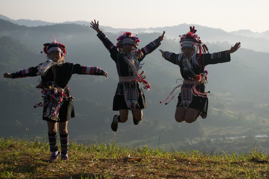 Tres niñas con trajes tradicionales de la tribu Akha saltando de alegría en una colina de Tailandia.