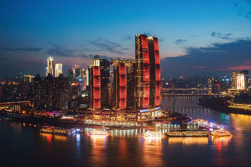 Complejo de rascacielos modernos iluminados con luces rojas y doradas junto al río Yangtsé en la ciudad de Chongqing durante la noche.