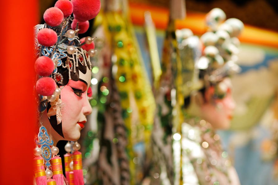 Primer plano de perfil de una actriz de ópera tradicional china luciendo un tocado ornamental detallado con pompones rojos y perlas
