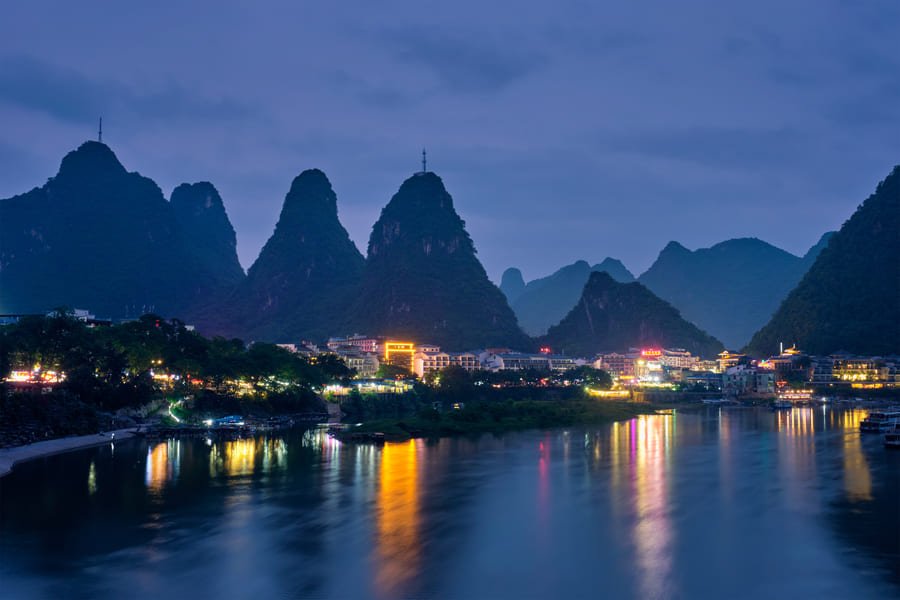 Vista nocturna iluminada del pueblo de Yangshuo junto al río Li con montañas kársticas al fondo en Guilin, China